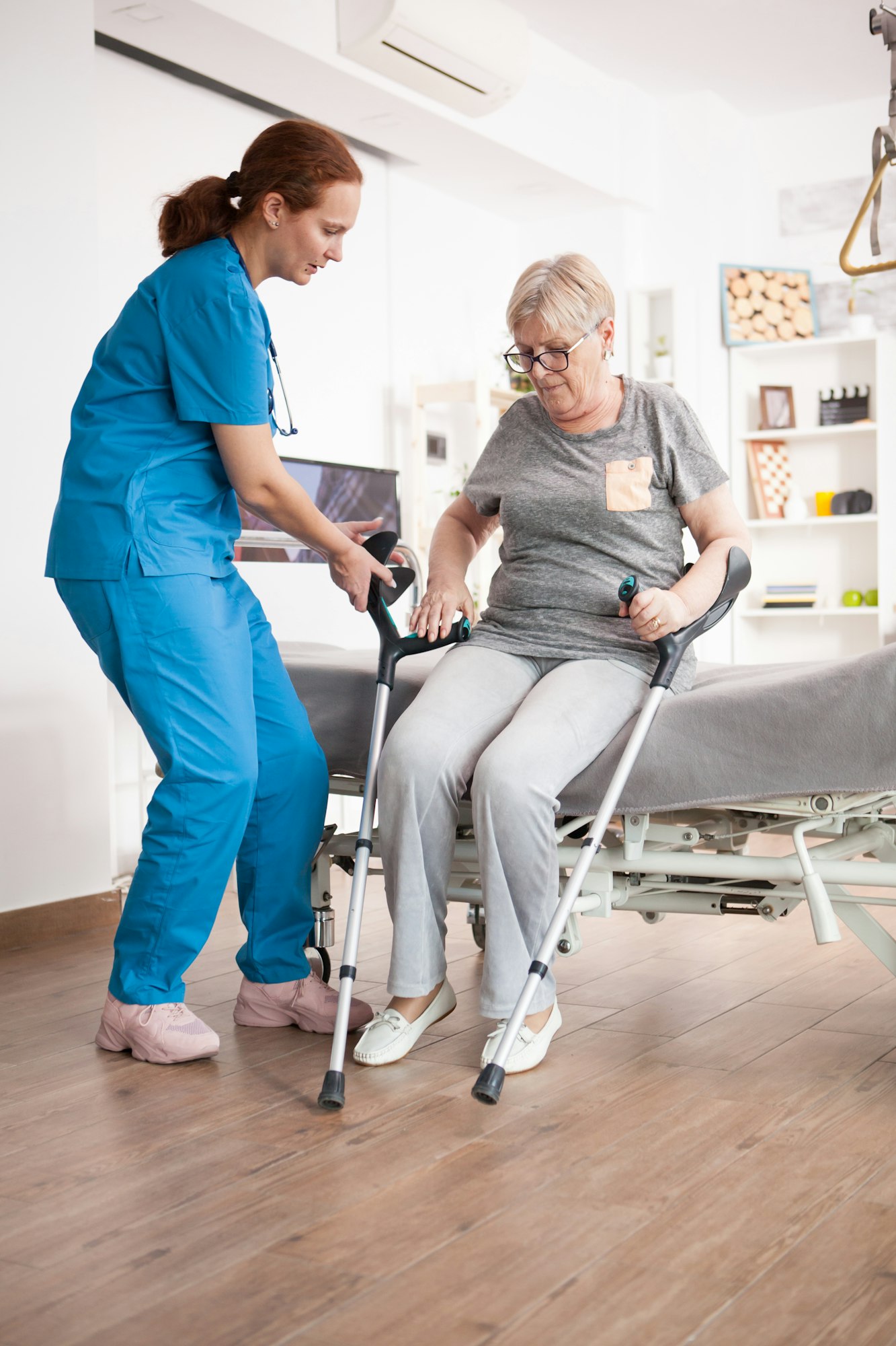 Nurse helping old woman to sit on bed in nursing home